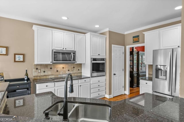 kitchen with a sink, white cabinets, appliances with stainless steel finishes, crown molding, and backsplash