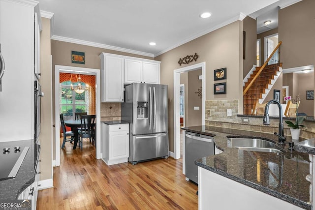 kitchen featuring dark stone countertops, light wood finished floors, a sink, white cabinets, and appliances with stainless steel finishes