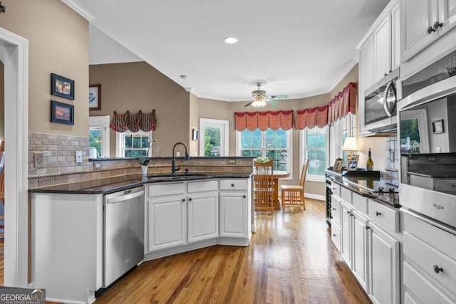 kitchen with light wood-style flooring, a peninsula, stainless steel appliances, a ceiling fan, and a sink