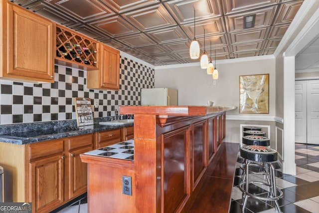 kitchen with an ornate ceiling, a kitchen island, freestanding refrigerator, brown cabinetry, and decorative backsplash