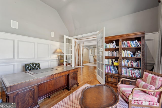 office featuring light wood-type flooring, a wainscoted wall, vaulted ceiling, and a decorative wall