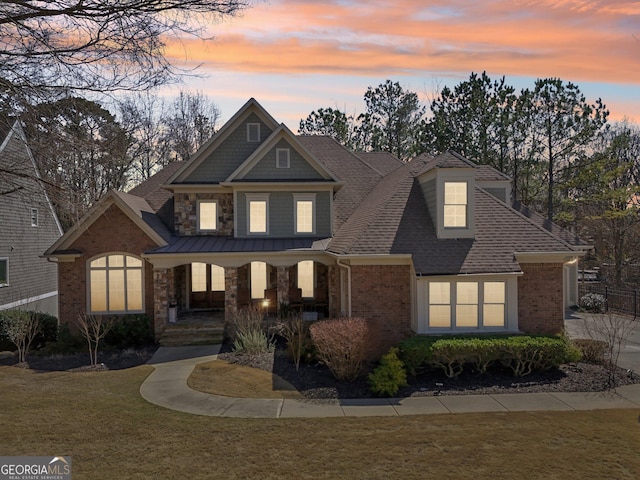 view of front of house featuring a front yard, a porch, brick siding, and stone siding