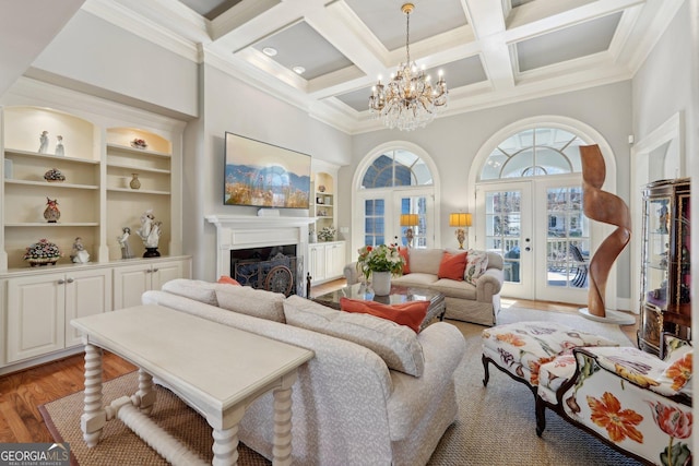 living area featuring beamed ceiling, light wood-style flooring, french doors, a high ceiling, and a notable chandelier