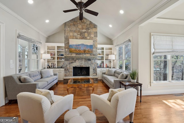 living area with wood finished floors, visible vents, a fireplace, ceiling fan, and crown molding