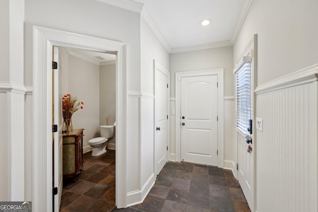 corridor featuring crown molding, a wainscoted wall, and stone finish flooring