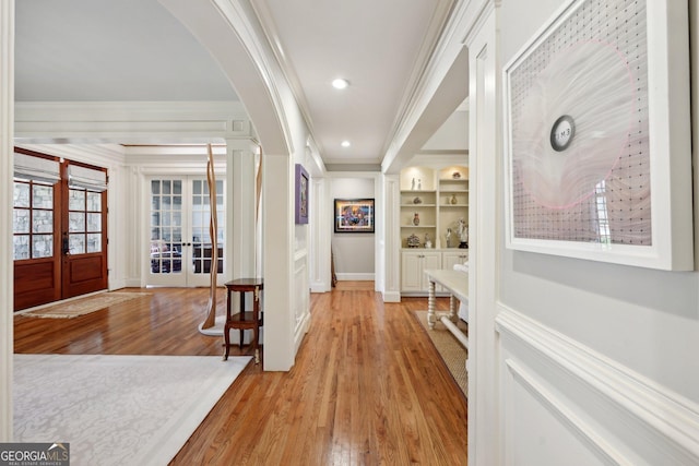 entryway with arched walkways, french doors, crown molding, and wood finished floors