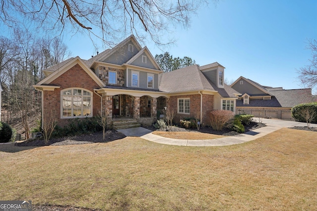 craftsman house featuring a front yard, a porch, fence, and brick siding