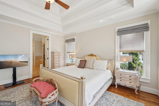 bedroom featuring a tray ceiling, wood finished floors, crown molding, baseboards, and ceiling fan