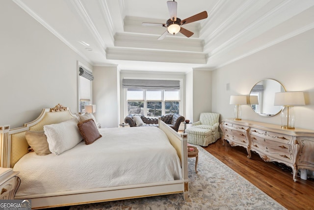 bedroom featuring ceiling fan, a tray ceiling, wood finished floors, and crown molding