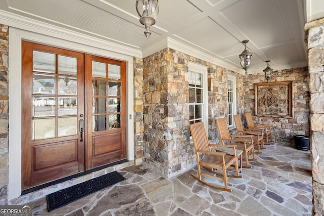 doorway to property featuring stone siding, a porch, and french doors