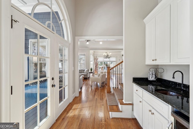 interior space featuring french doors, light wood-style floors, an inviting chandelier, a towering ceiling, and stairs