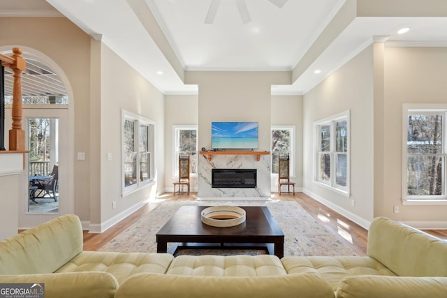 living room with crown molding, baseboards, ceiling fan, a fireplace, and wood finished floors