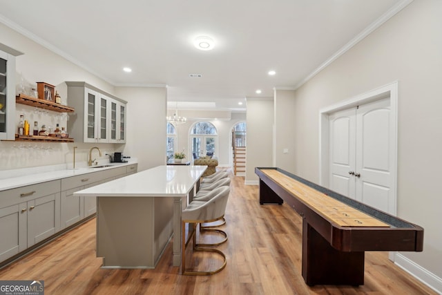 bar with baseboards, light wood-style flooring, a sink, crown molding, and a notable chandelier