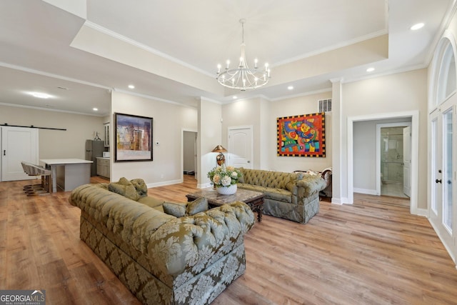 living area featuring an inviting chandelier, a tray ceiling, a barn door, and light wood finished floors