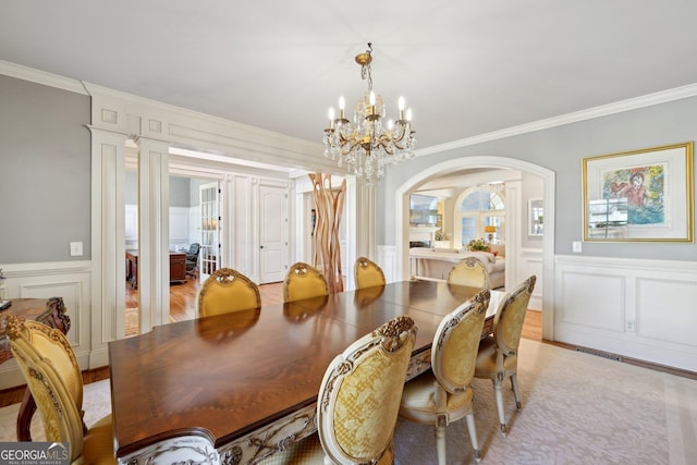 dining room with arched walkways, a chandelier, crown molding, and a decorative wall