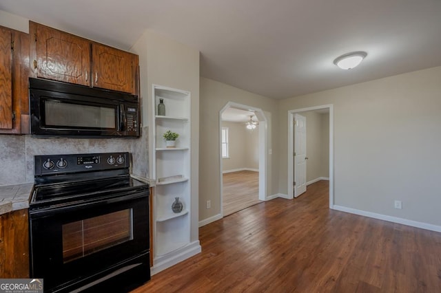 kitchen featuring baseboards, brown cabinets, arched walkways, black appliances, and dark wood-style flooring