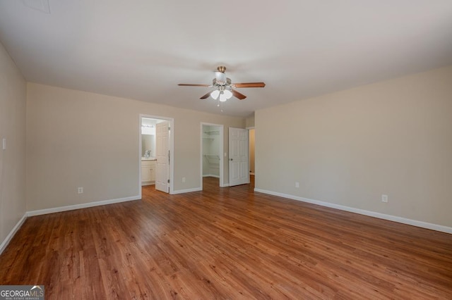 unfurnished bedroom featuring a walk in closet, a ceiling fan, wood finished floors, a closet, and baseboards