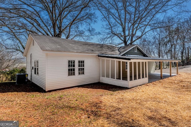 back of property with a carport, cooling unit, a sunroom, and roof with shingles