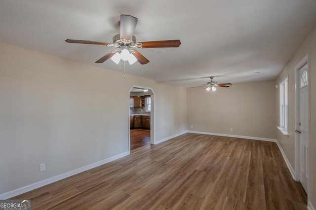 spare room with arched walkways, baseboards, a ceiling fan, and wood finished floors