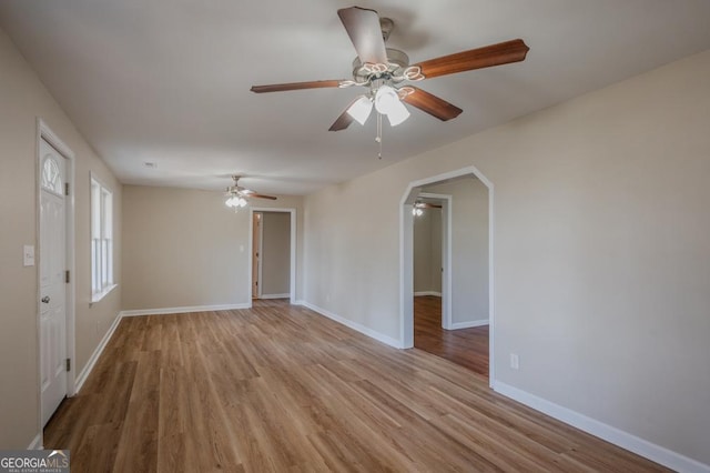 empty room with ceiling fan, wood finished floors, arched walkways, and baseboards