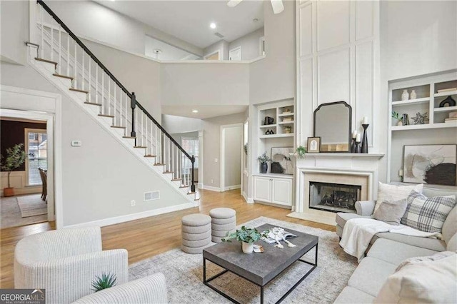 living area featuring built in features, light wood-type flooring, a high ceiling, and stairs