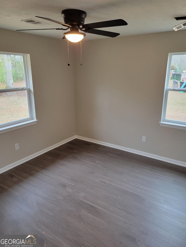 unfurnished room with a wealth of natural light, visible vents, dark wood finished floors, and a ceiling fan