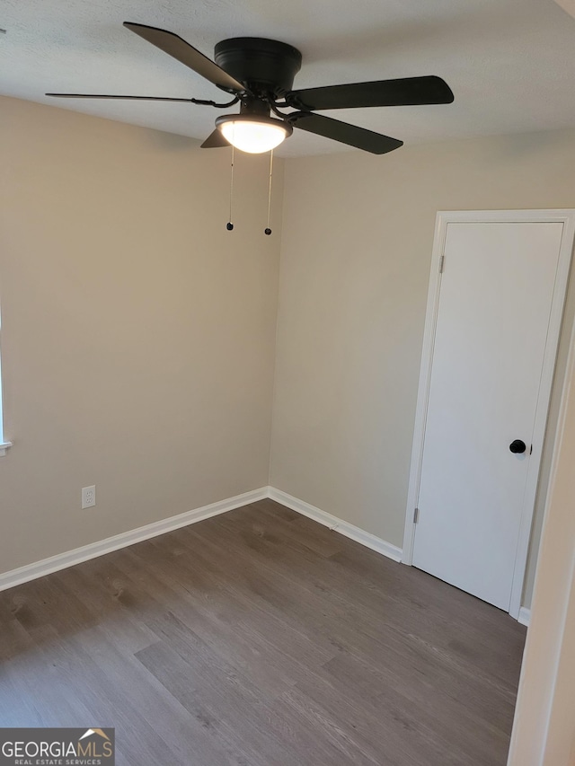 unfurnished room featuring baseboards, dark wood-type flooring, and a ceiling fan