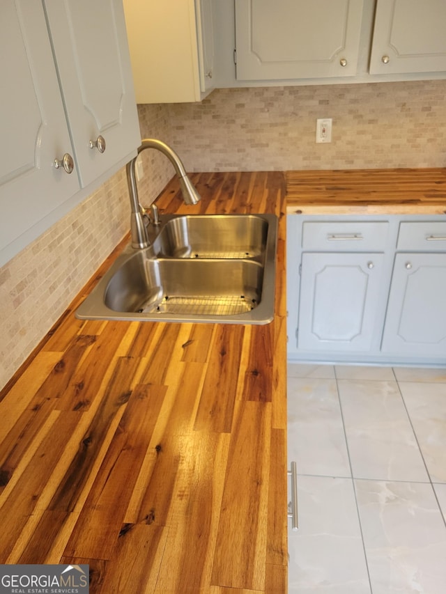 kitchen featuring decorative backsplash, butcher block counters, white cabinetry, and a sink