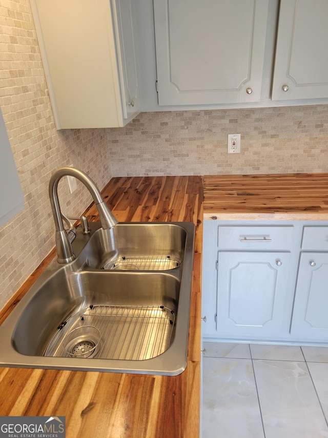 kitchen featuring wood counters, white cabinetry, backsplash, and a sink