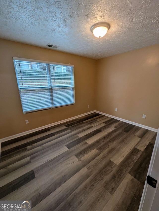 unfurnished room with dark wood finished floors, baseboards, visible vents, and a textured ceiling