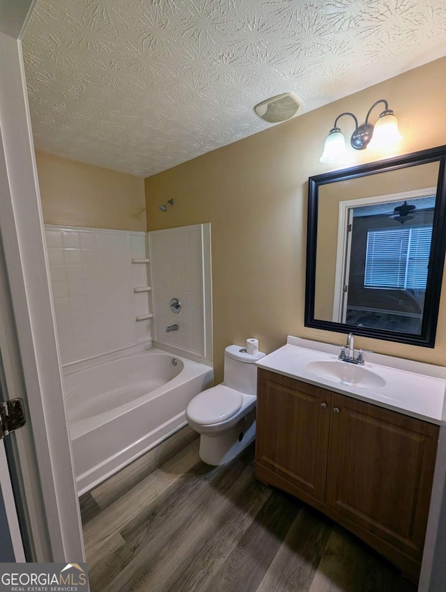 full bath featuring vanity, wood finished floors,  shower combination, a textured ceiling, and toilet