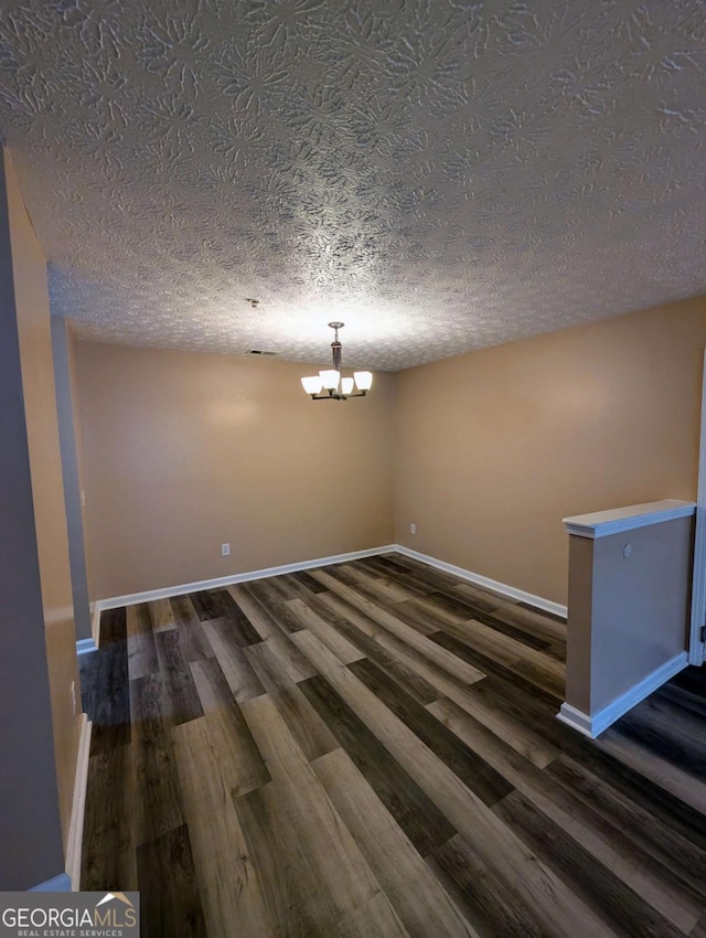 unfurnished dining area with baseboards, a textured ceiling, an inviting chandelier, and dark wood finished floors