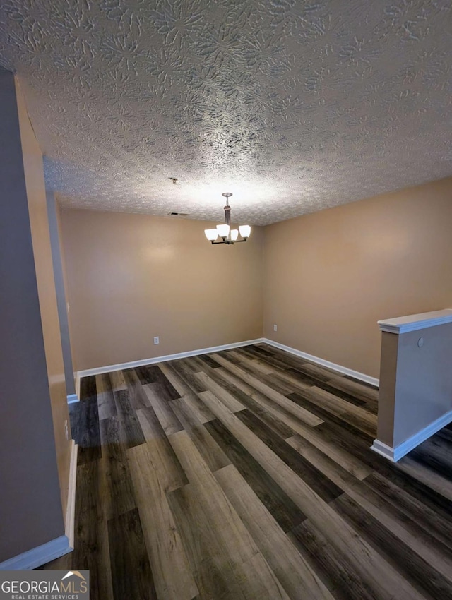 unfurnished dining area featuring dark wood finished floors, a textured ceiling, baseboards, and an inviting chandelier