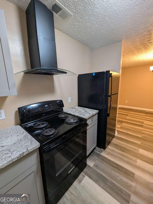 kitchen featuring visible vents, light wood-style flooring, black appliances, and wall chimney exhaust hood