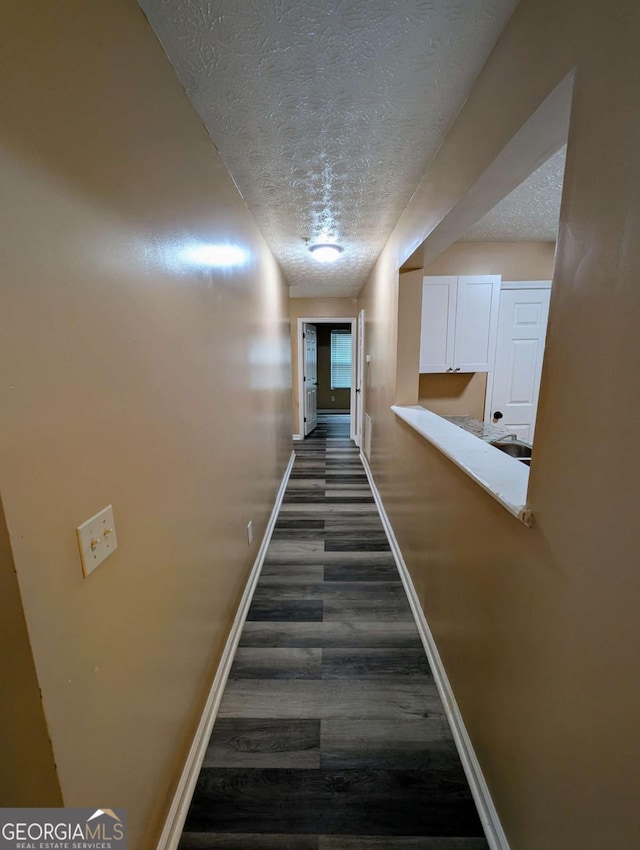 hallway with baseboards, a textured ceiling, and dark wood-type flooring