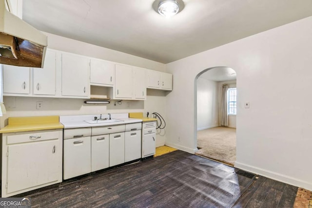 kitchen featuring a sink, white cabinetry, arched walkways, baseboards, and dark wood-style flooring