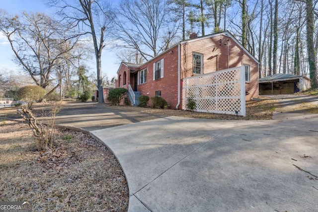 view of side of home featuring brick siding, a chimney, and concrete driveway