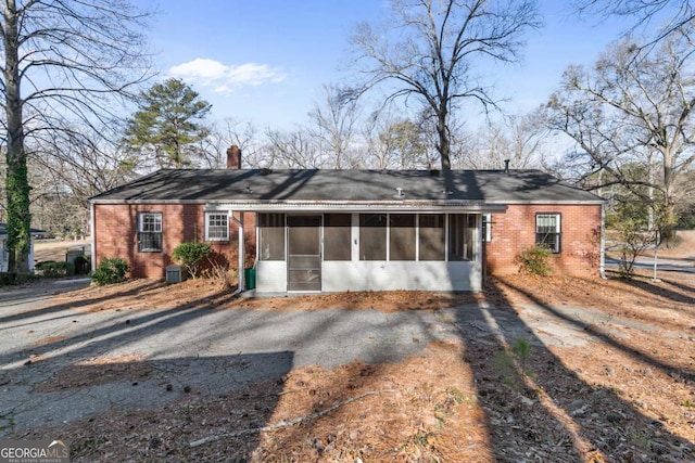 single story home featuring brick siding, central AC unit, a chimney, and a sunroom