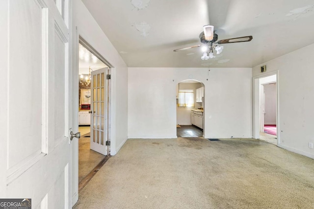 empty room featuring baseboards, arched walkways, carpet, and ceiling fan with notable chandelier