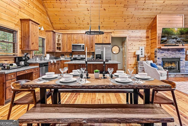 dining area with light wood finished floors, wooden walls, wood ceiling, a fireplace, and high vaulted ceiling