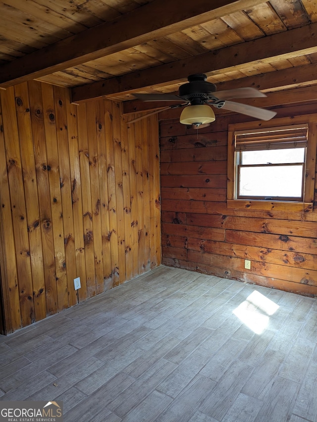 empty room with wooden walls, beamed ceiling, wooden ceiling, wood finished floors, and a ceiling fan