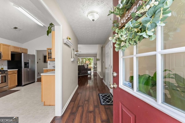 corridor with visible vents, a textured ceiling, baseboards, and wood finished floors