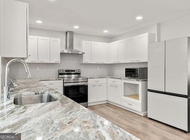 kitchen featuring stainless steel electric range oven, light stone counters, a sink, wall chimney exhaust hood, and white refrigerator