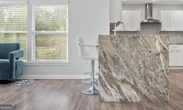 details with white cabinetry, wood finished floors, wall chimney exhaust hood, and light stone countertops