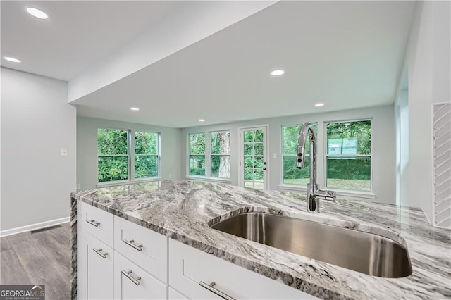 kitchen featuring light stone counters, recessed lighting, wood finished floors, white cabinetry, and a sink