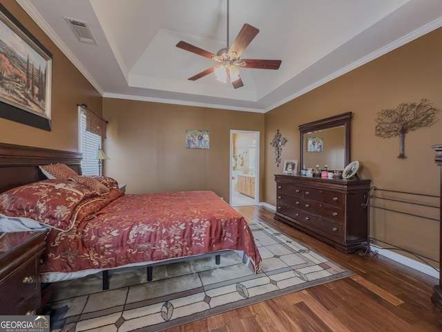 bedroom with wood finished floors, visible vents, ornamental molding, ensuite bathroom, and a raised ceiling