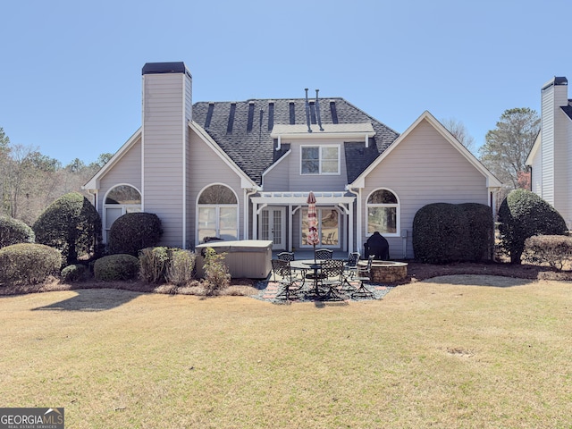 rear view of house with a lawn, a hot tub, roof with shingles, a chimney, and a patio area