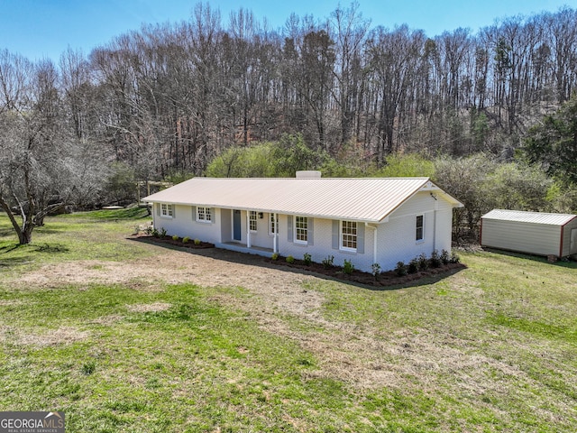 ranch-style home featuring a front lawn, a storage shed, an outdoor structure, metal roof, and brick siding