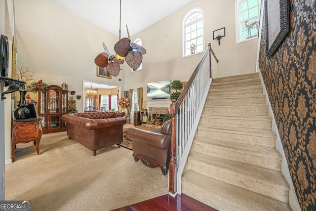 stairway featuring ceiling fan with notable chandelier, a fireplace, a high ceiling, and carpet