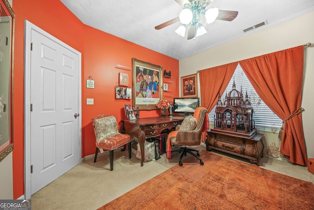 office area with a textured ceiling, visible vents, carpet floors, and ceiling fan